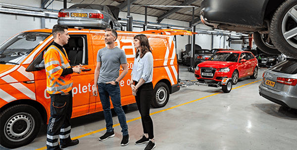 A man and a woman talking to an RAC mechanic in a garage