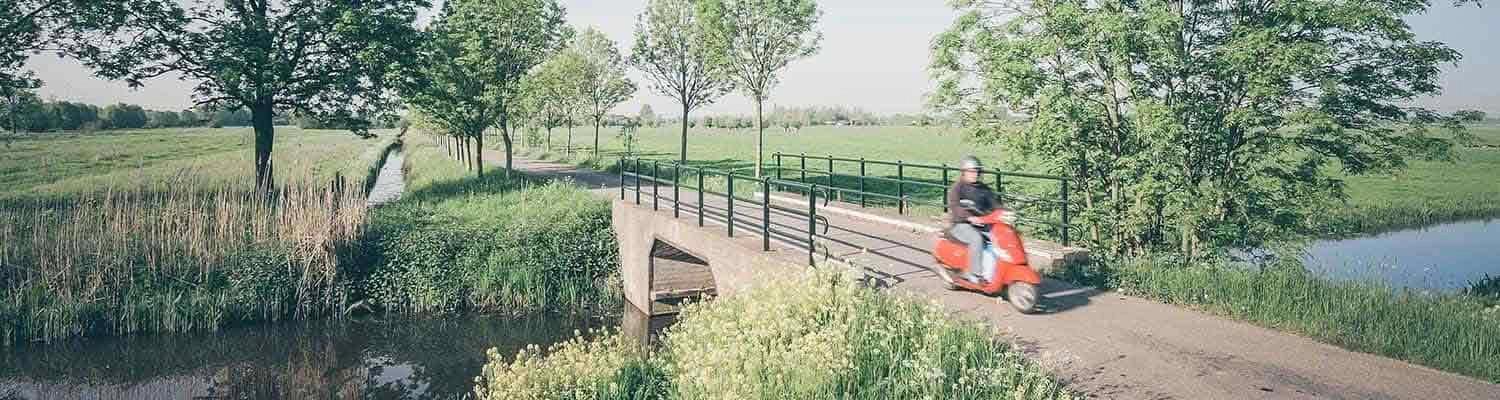 Person riding red moped across water bridge